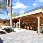 Luxe vakantiehuis De Groene Lantaarn buitenruimte met houten overkapping, eettafels en bartafel.