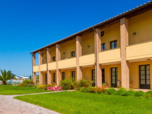 salvapiano appartementen Italie Een geel appartementenblok bij Salvapiano Holiday ranch omgeven door gras en bloemen