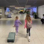 Koffer inpakken voor een vakantie met kinderen. 2 kinderen met koffer op vliegveld